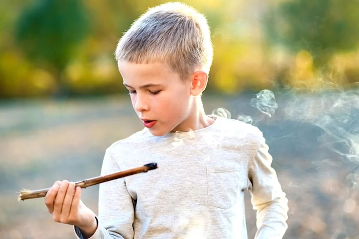 Chłopiec bawi się paląc drewniany kij na zewnątrz