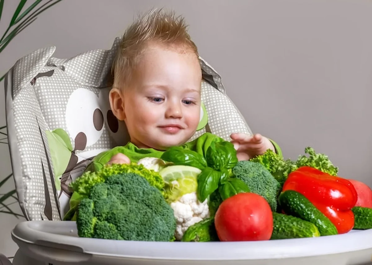 Maluch siedzi na dziecięcym krześle i wybiera warzywa do jedzenia